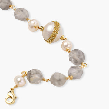 Bracelet with cloudy quartz beads, freshwater pearls, and gold-wrapped baroque pearl centerpiece on white background.