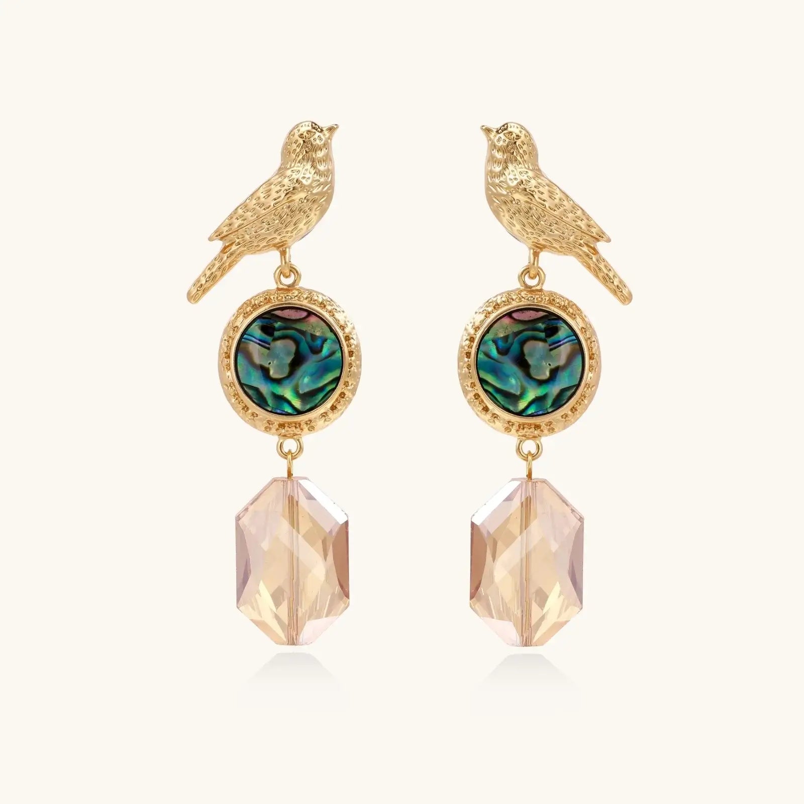 Gold-plated bird stud earrings with iridescent abalone shell medallions and champagne crystal drops on cream background