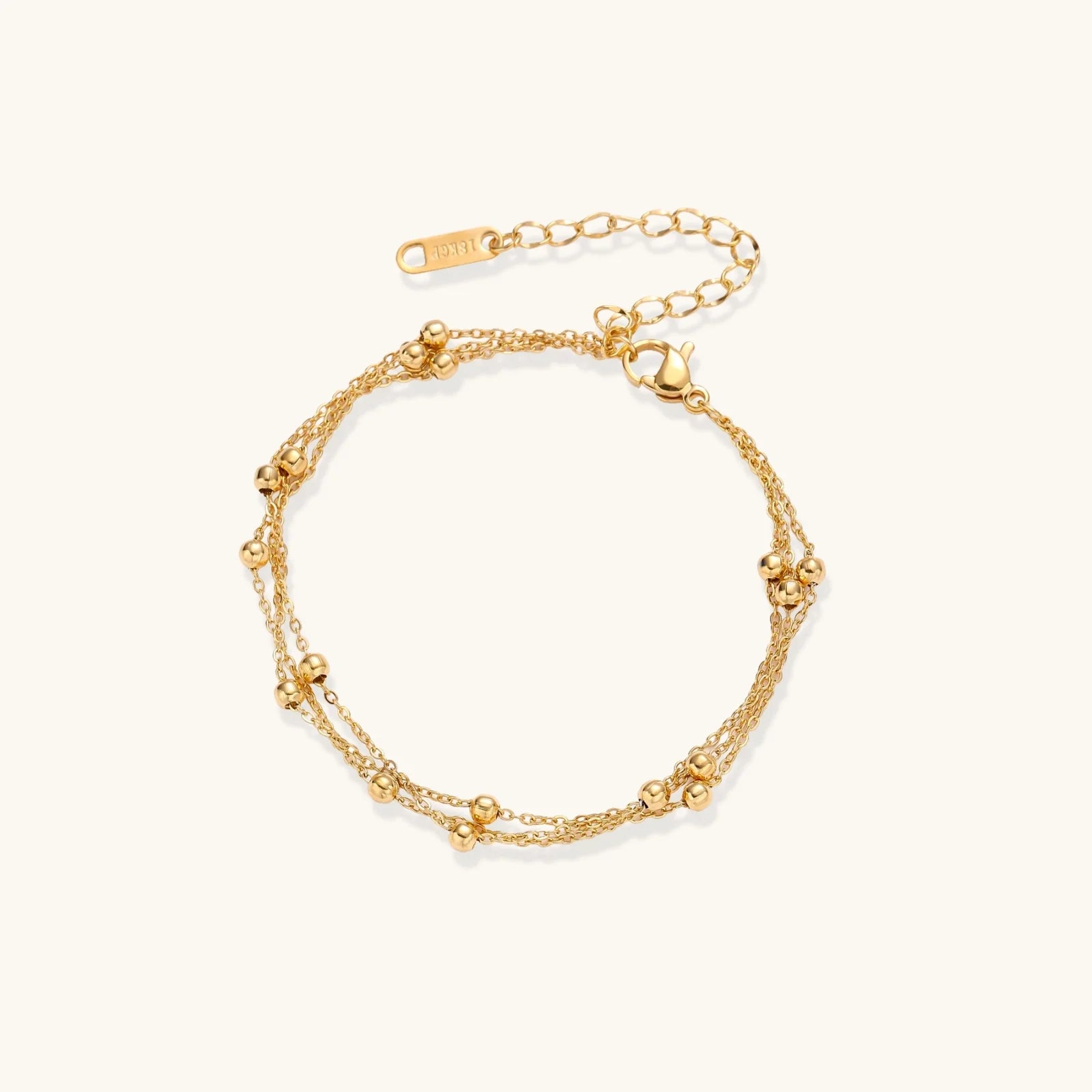 Three-strand gold-plated bracelet with clustered ball beads and adjustable clasp on cream background