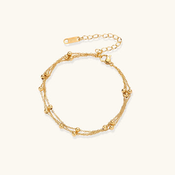 Three-strand gold-plated bracelet with clustered ball beads and adjustable clasp on cream background
